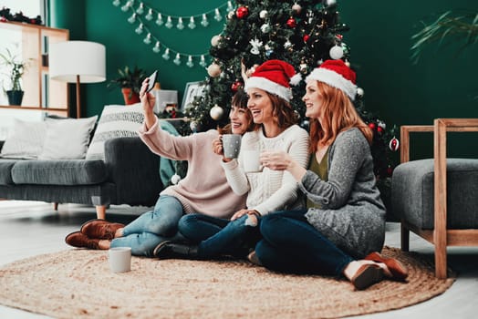 Capturing memories. three attractive middle aged women taking self portraits together with a cellphone at home during Christmas time