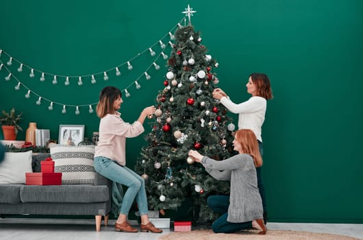 Little traditions for future generations. three attractive women decorating a Christmas tree together at home