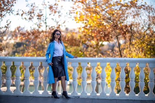 Woman autumn city, lifestyle. A middle-aged woman in a blue raincoat, black leather skirt and white blouse walks through the autumn city