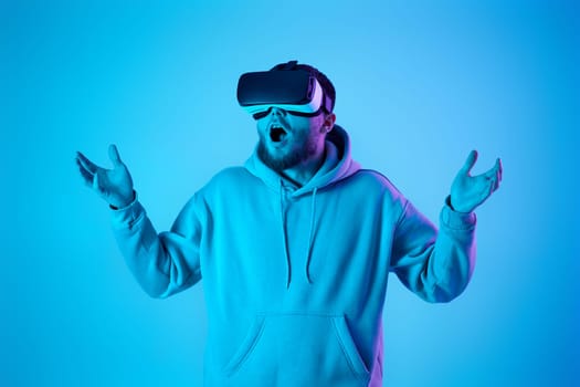 man in sweatshirt using virtual reality glasses and playing video games on blue background. Neon lighting