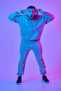 handsome bearded man with headphones in sweatshirt enjoying favorite music on purple neon background. Neon lighting