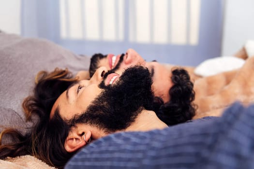 happy gay male couple smiling lying on the bed with their faces together, concept of real people lifestyle at home and love between people of the same sex