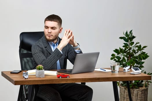 young man sitting on chair at table and resting, using laptop on white wall background