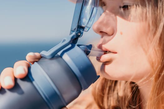 Fintess woman drinking water. Happy, active middle aged woman standing on beach and drinking water after excersise. Concept of lifestyle, sport. Close up.