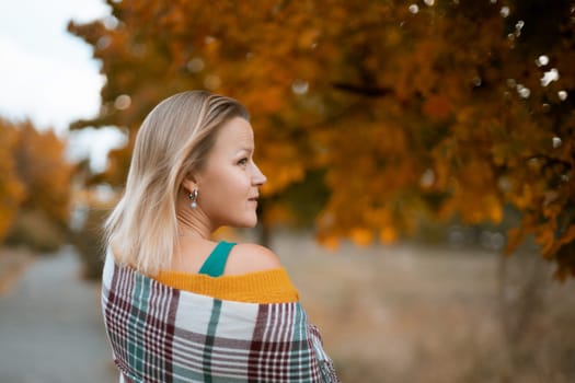 autumn woman in a green dress, plaid, against the background of an autumn tree.