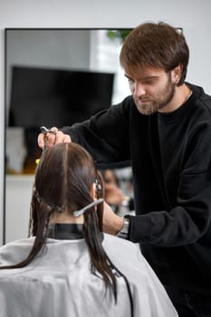 Professional male hairdresser with scissors cutting female hair in salon