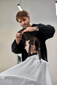 Professional male hairdresser with scissors cutting female hair in salon