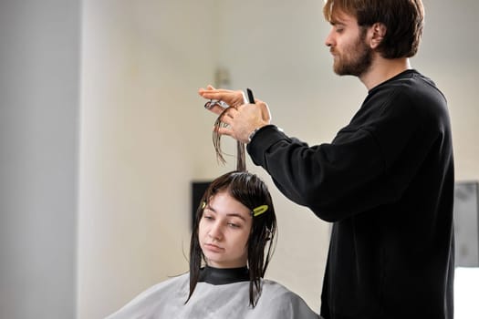 Professional male hairdresser with scissors cutting female hair in salon