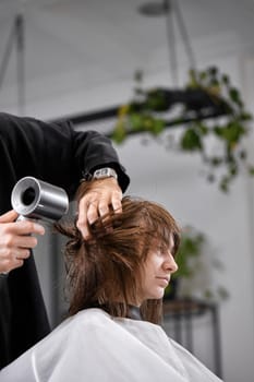 man hairdresser using hair dryer for female hair after washing in the beauty salon.