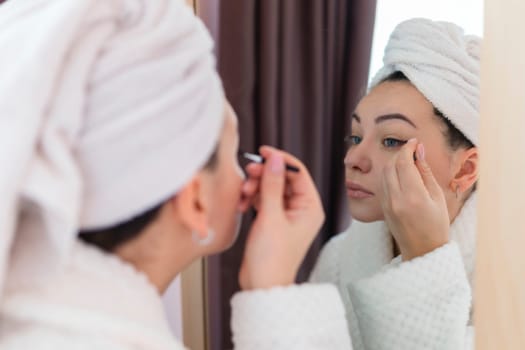 A woman applies black mascara to her eyelashes with a makeup brush. Young beautiful woman applying mascara makeup on her eyes in the bathroom.