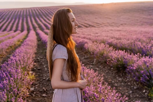 Woman lavender field sunset. Romantic woman walks through the lavender fields. illuminated by sunset sunlight. She is wearing a pink dress with a hat