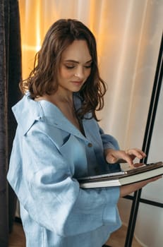 A young woman in a dark blue suit stands in a room with a tablet in her hands. Browses online stores, social networks. Vertical frame.