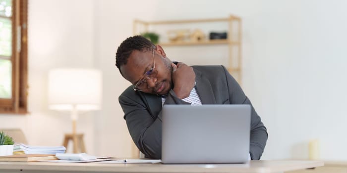 Tired American African business man in stress works with many paperwork document. migraine attack. Freelance, work from home.