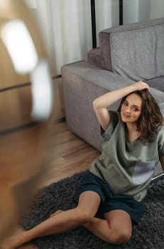 Portrait of a beautiful woman who sits indoors on the floor, straightens her hair. View from above.