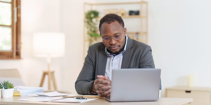 Tired American African business man in stress works with many paperwork document. migraine attack. Freelance, work from home.