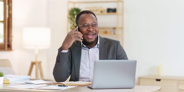 Smiling American African Banker or Accountant talking phone with client and makes financial report and studies annual figures, analyzes profits.