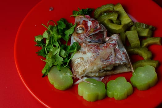 Steamed red snapper head with bitter gourds and chayotes on red plate. Studio shot. Selective focus. Copy space.