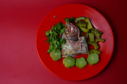 Steamed red snapper head with bitter gourds and chayotes on red plate. Studio shot. Selective focus. Copy space.