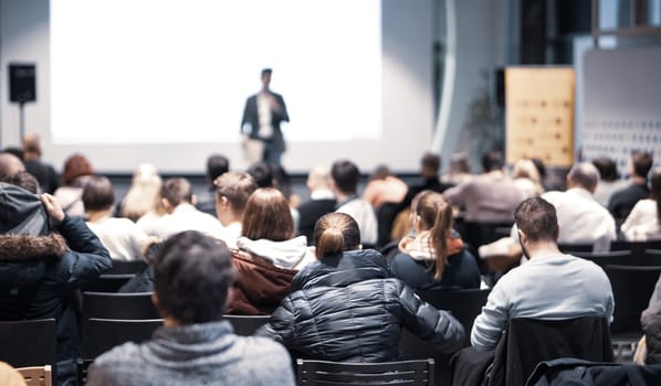 Speaker giving a talk in conference hall at business event. Rear view of unrecognizable people in audience at the conference hall. Business and entrepreneurship concept.