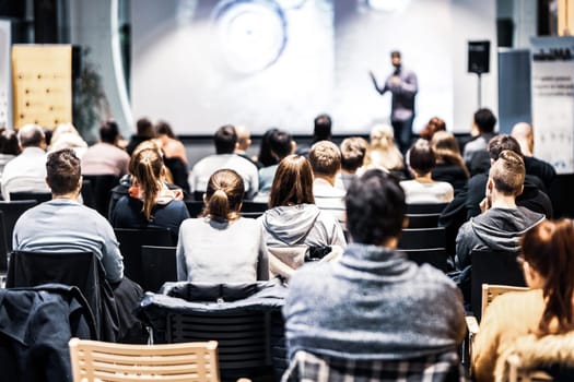 Speaker giving a talk in conference hall at business event. Audience at the conference hall. Business and Entrepreneurship concept. Focus on unrecognizable people in audience.