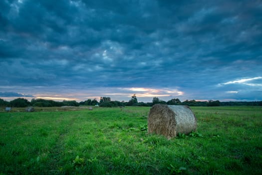 Bale of hay in the meadow and cloudy sky, summer evening