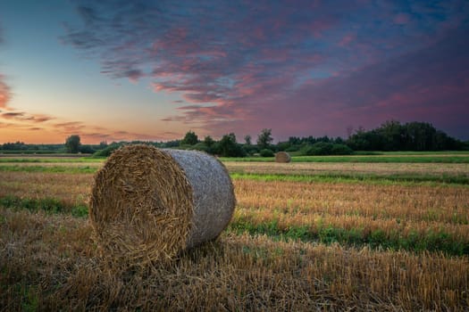 One hay bale in the field and colorful clouds during sunset