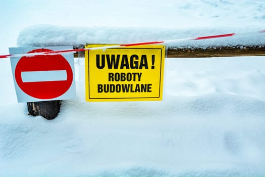 No entry sign on the fence and yellow in Polish, Attention Works, winter snowy day