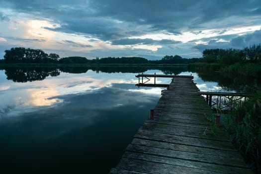 Wooden pier on a calm lake and evening dramatic clouds