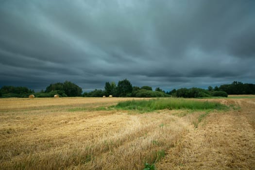Dark storm clouds over stubble field, summer day, eastern Poland