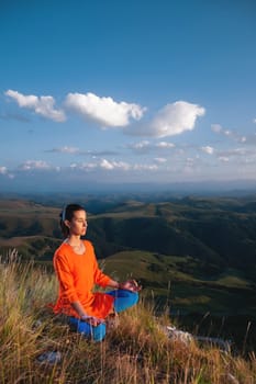 a woman sits facing the sun and meditates in the lotus position next to a cliff in the mountains. fresh air and inspiration.