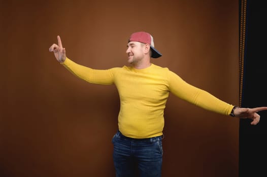 Portrait of a happy handsome man in casual clothes dancing in the studio. Cheerful attractive man in yellow t-shirt and cap dancing and having fun.