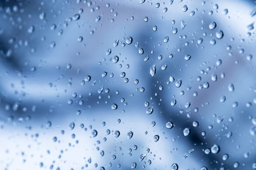 natural water drops on the window glass. blue background with rain on the window, close-up.