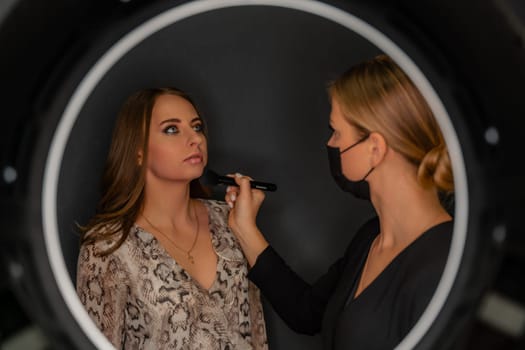 Makeup beauty salon. Makeup artist applies powder and blush. Beautiful female face. Makeup master's hand puts blush on cheeks of beauty model girl. Makeup in progress.