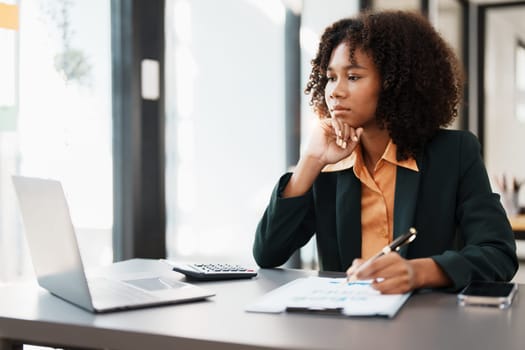 Beautiful young teen American African holding computer laptop with planning working on financial document, tax, exchange, accounting and Financial advisor.