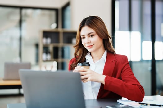 Beautiful young teen asian businesswomen using computer laptop and drink coffee with in smile winner is gesture, Happy to be successful celebrating achievement success.