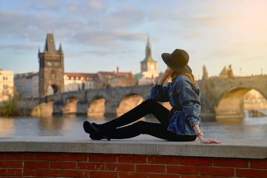 Stylish young beautiful woman earing black hat in Prague with Charles Bridge on background. Elegant retro lady fine art portrait.