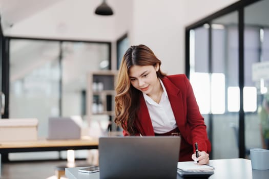 Beautiful young teen asian businesswoman using laptop computer and paperworks with planning working on financial document, tax, exchange, accounting and Financial advisor.