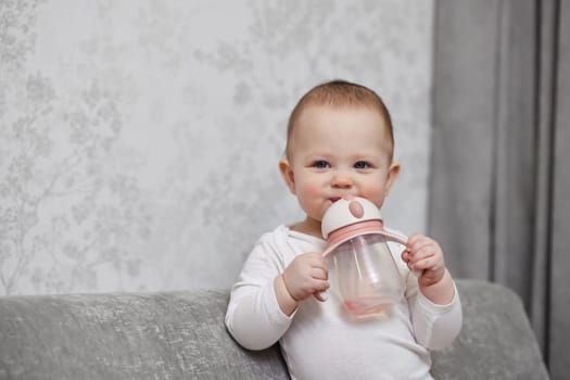 little child girl holding bottle and drinking water at home.