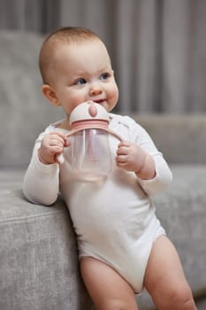 cute baby girl holding bottle and drinking water at home.