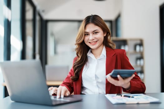 Beautiful young teen asian businesswoman using computer laptop and calculator for calculate with planning working on financial document, tax, exchange, accounting and Financial advisor.