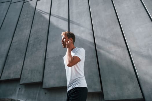 Against building exterior. Young man in sportive clothes have workout outdoors at daytime.