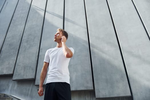 Against building exterior. Young man in sportive clothes have workout outdoors at daytime.