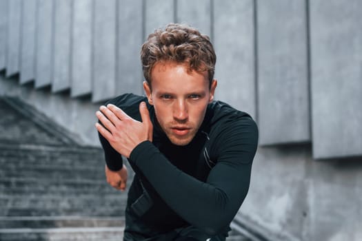 Runs forward. Young man in sportive clothes have workout outdoors at daytime.