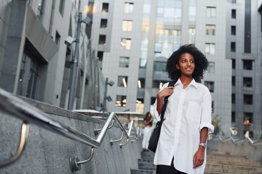 African american woman in good clothes is outdoors in the city at daytime.