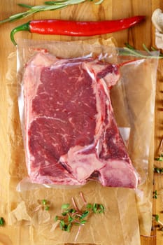 Raw meat in vacuum packaging on a wooden board with spices. Top view. Vertical photo