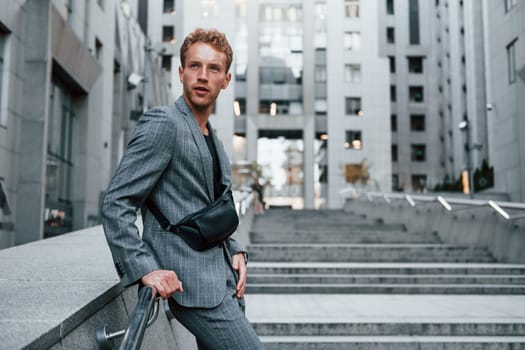 Young elegant man in good clothes is outdoors in the city at daytime.