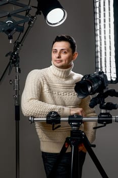 Professional handsome photographer with digital camera on tripod on gray background with lighting equipment