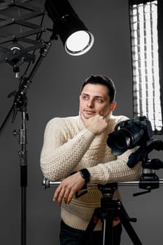 Professional handsome photographer with digital camera on tripod on gray background with lighting equipment