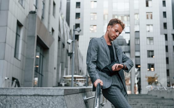 Young elegant man in good clothes is outdoors in the city at daytime.