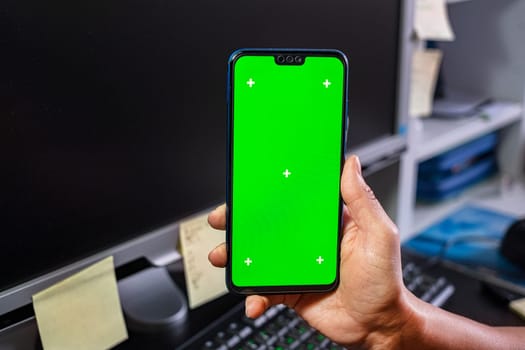 Woman hands hold a smartphone with green screen of workspace background. Chroma key phone. Successful sales strategy.